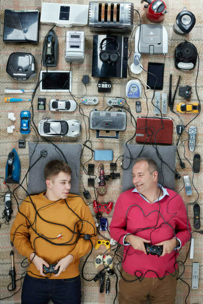 A man and a boy lying down amongst a lot of electrical goods