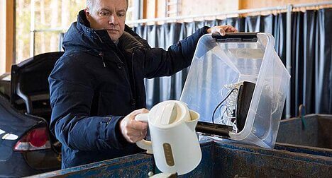 A middle-age light skinned man unpacking an electric kettle at a recycling centre from a plastic box