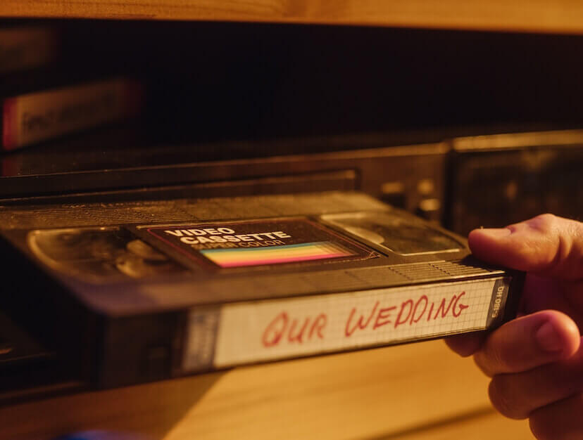 A video tape is being inserted into a VHS player with the text 'Our wedding' on the video label.