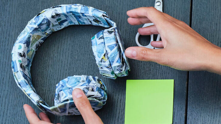 hands reaching for headphones made from origami bank notes