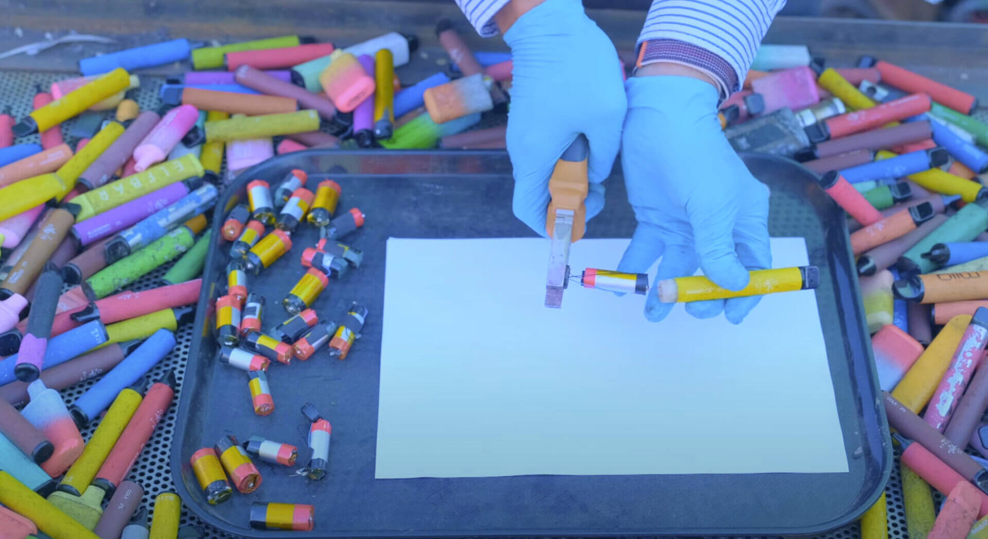 two hands in blue rubber gloves pulling a single use vape apart for recycling