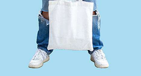 a person holding a white tote bag between their legs against a blue background