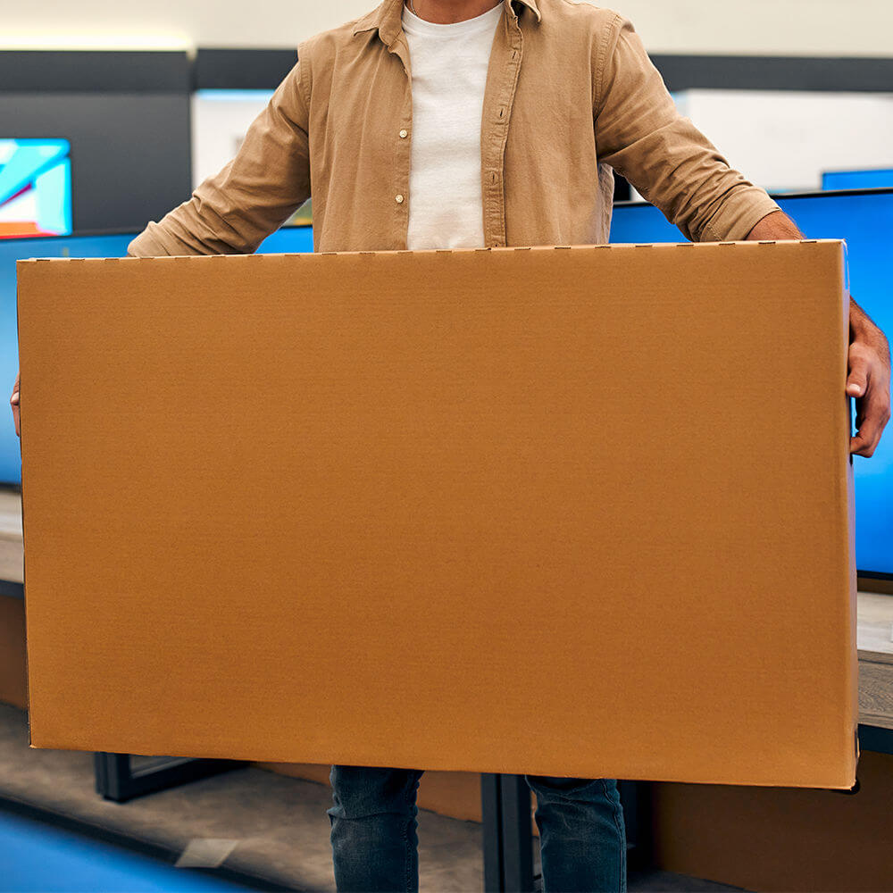light skinned man holding a very large cardboard box with a TV inside.