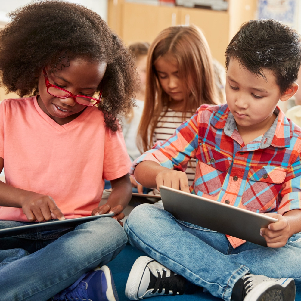 Three children sitting cross legged in a classroom using tablets