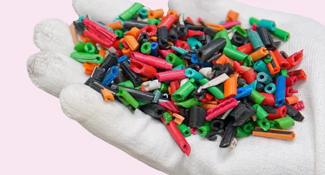 close up of gloved hand holding multi-coloured plastic nurdles