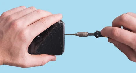 Close up of a light skinned person holding a smart phone in their left hand and a mini screwdriver in their right hand which is connected to the bottom of the phone.