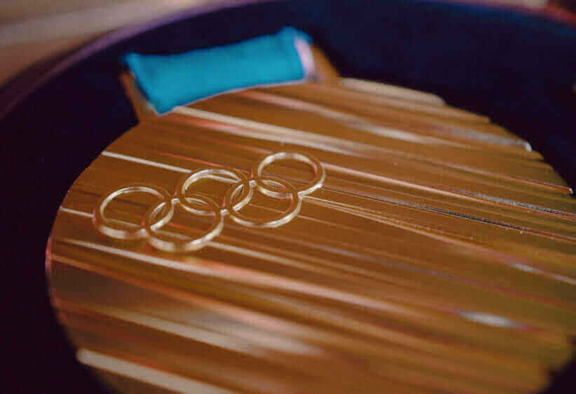 Japan medal marvin-ronsdorf-pw29v3PzSaw-unsplash1-e1601387689125 882x562 px a close up of a gold Olympic medal with the five Olympic rings and the blue band